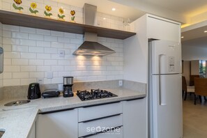 A modern kitchen with white cabinets, a gas stove, a built-in oven, and a refrigerator. - Charming Apartment With Barbecue Por0101 (Florianópolis)