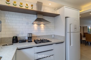 A modern kitchen with white cabinets, a gas stove, a built-in oven, and a refrigerator. - Charming Apartment With Barbecue Por0101 (Florianópolis)