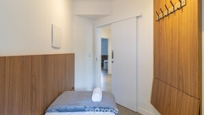 Ein modernes Hotelzimmer mit einem hölzernen Kopfteil, einem ordentlich bezogenen Bett mit einem zusammengerollten Handtuch, einem an der Wand befestigten Kleiderhaken und einer Schiebetür zu einem Badezimmer.
