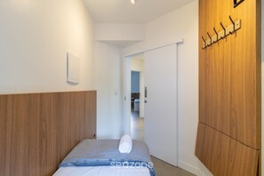 A modern hotel room with a wooden headboard, a neatly made bed with a rolled towel, a wall-mounted coat rack, and a sliding door leading to a bathroom. - Charming Apartment With Barbecue Por0101 (Florianópolis)
