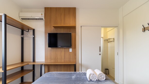 Ein modernes Schlafzimmer mit einem Bett, einem an einer Holzplatte montierten Fernseher und einem Kleiderschrank mit Kleiderstange.