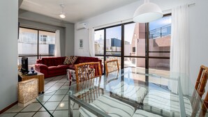 A modern living room with a glass dining table, red sofa, and wicker chairs. - Exclusive Penthouse in Florianopolis Por410 (Florianópolis)
