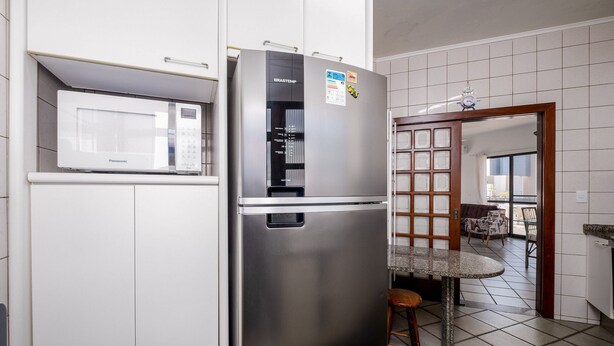 A kitchen with a stainless steel refrigerator, a microwave, and a dining area with a table and chairs. - Exclusive Penthouse in Florianopolis Por410 (Florianópolis)