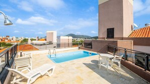 A rooftop pool area with a clear view of the cityscape and mountains in the background. - Exclusive Penthouse in Florianopolis Por410 (Florianópolis)