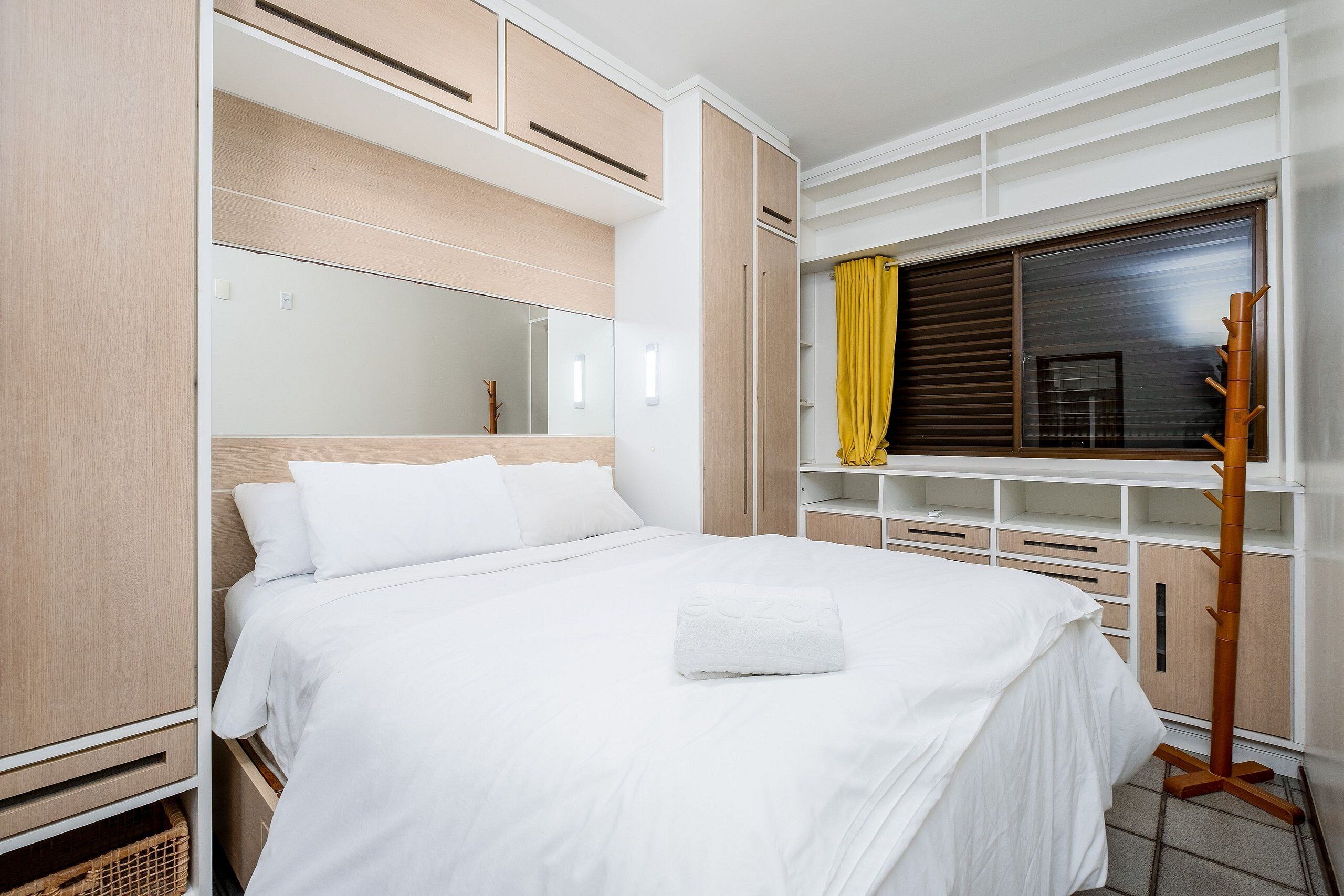 A neatly arranged bedroom with a bed, a wardrobe, a mirror, and a window with curtains.