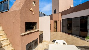 A modern outdoor patio area with a built-in grill, a white table, and a staircase leading to an upper level. - Exclusive Penthouse in Florianopolis Por410 (Florianópolis)