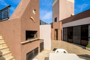 Ein moderner Außenbereich mit Terrasse, einem eingebauten Grill, einem weißen Tisch und einer Treppe zu einer erhöhten Ebene.