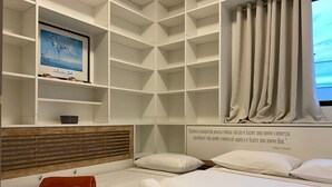 A hotel room with a bed, a wooden headboard, a shelf with a framed picture, a window with curtains, and a quote on the wall. - Exclusive Penthouse in Florianopolis Por410 (Florianópolis)