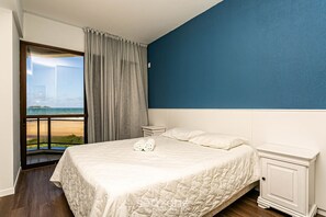 A bedroom with a large bed, a nightstand, and a view of the beach through a window. - Apto With Panoramic View of the sea Front Por204 (Florianópolis)