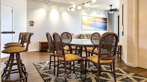 A dining area with a round table, six wicker chairs with yellow cushions, a hanging light fixture, and a painting on the wall. - Apto With Panoramic View of the sea Front Por204 (Florianópolis)
