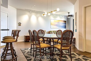 A dining area with a round table, six wicker chairs with yellow cushions, a hanging light fixture, and a painting on the wall. - Apto With Panoramic View of the sea Front Por204 (Florianópolis)