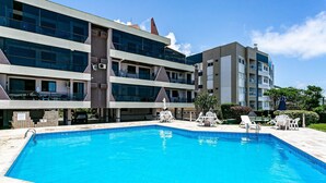 A modern hotel with a swimming pool, outdoor seating, and a multi-story building with balconies. - Apto With Panoramic View of the sea Front Por204 (Florianópolis)