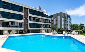 A modern hotel with a swimming pool, outdoor seating, and a multi-story building with balconies. - Apto With Panoramic View of the sea Front Por204 (Florianópolis)