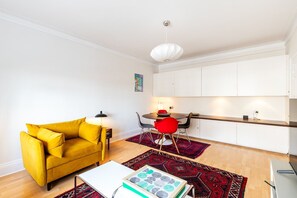 Un espace de vie moderne avec un canapé jaune, une table à manger avec des chaises rouges et un coin cuisine doté de meubles blancs.