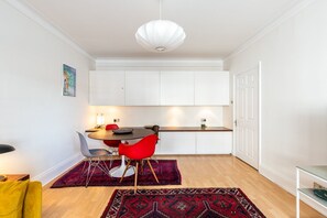 Une cuisine compacte avec des meubles blancs, une table à manger entourée de chaises rouges et un luminaire suspendu.