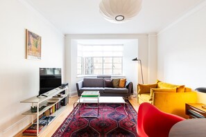 Ein Wohnzimmer mit einer Couch, einem roten Sessel, einem Couchtisch, einem Fernseher und einem Bücherregal.