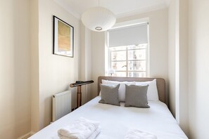 Une chambre d’hôtel avec un lit, un radiateur, un chauffage d’appoint, une fenêtre avec des stores et un tableau encadré au mur.