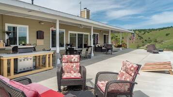 An outdoor patio area with a covered seating arrangement, a grill station, and a view of a hilly landscape.