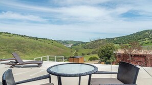 A patio with a round table and chairs, overlooking a valley with a small building and a wooden fence. - The J's Nest Deluxe by Avantstay Sleeps 18 Hot Tub + Game Room Paso Robles (Bradley)