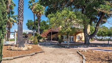 A building with a covered patio, palm trees, and a dirt path.