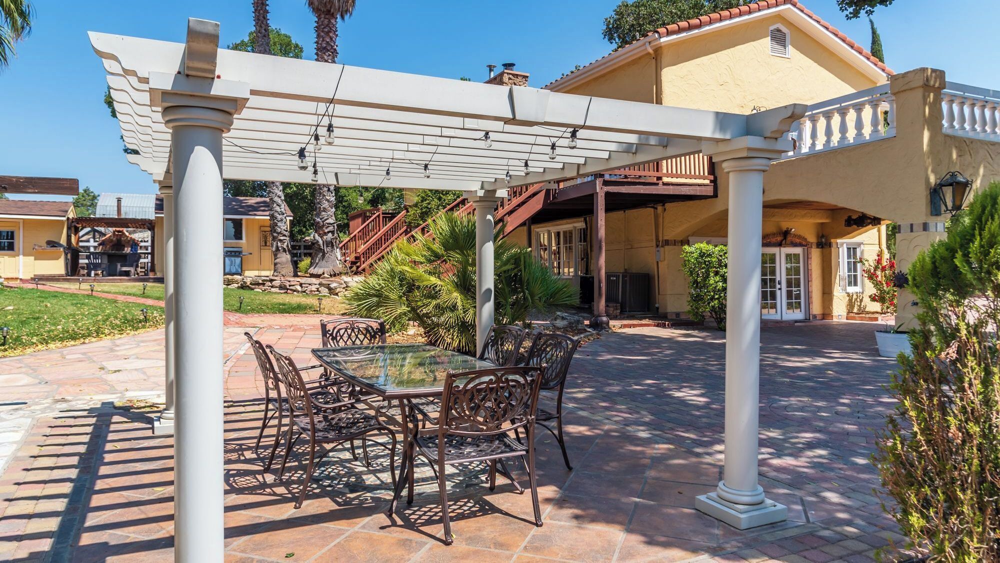 A covered patio with a table and chairs, a pergola, and a staircase leading to a building.