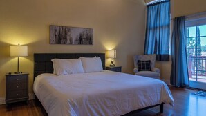 Una camera d'albergo con un letto grande, due comodini con lampade, una sedia, un quadro appeso e vista attraverso una finestra con tende.