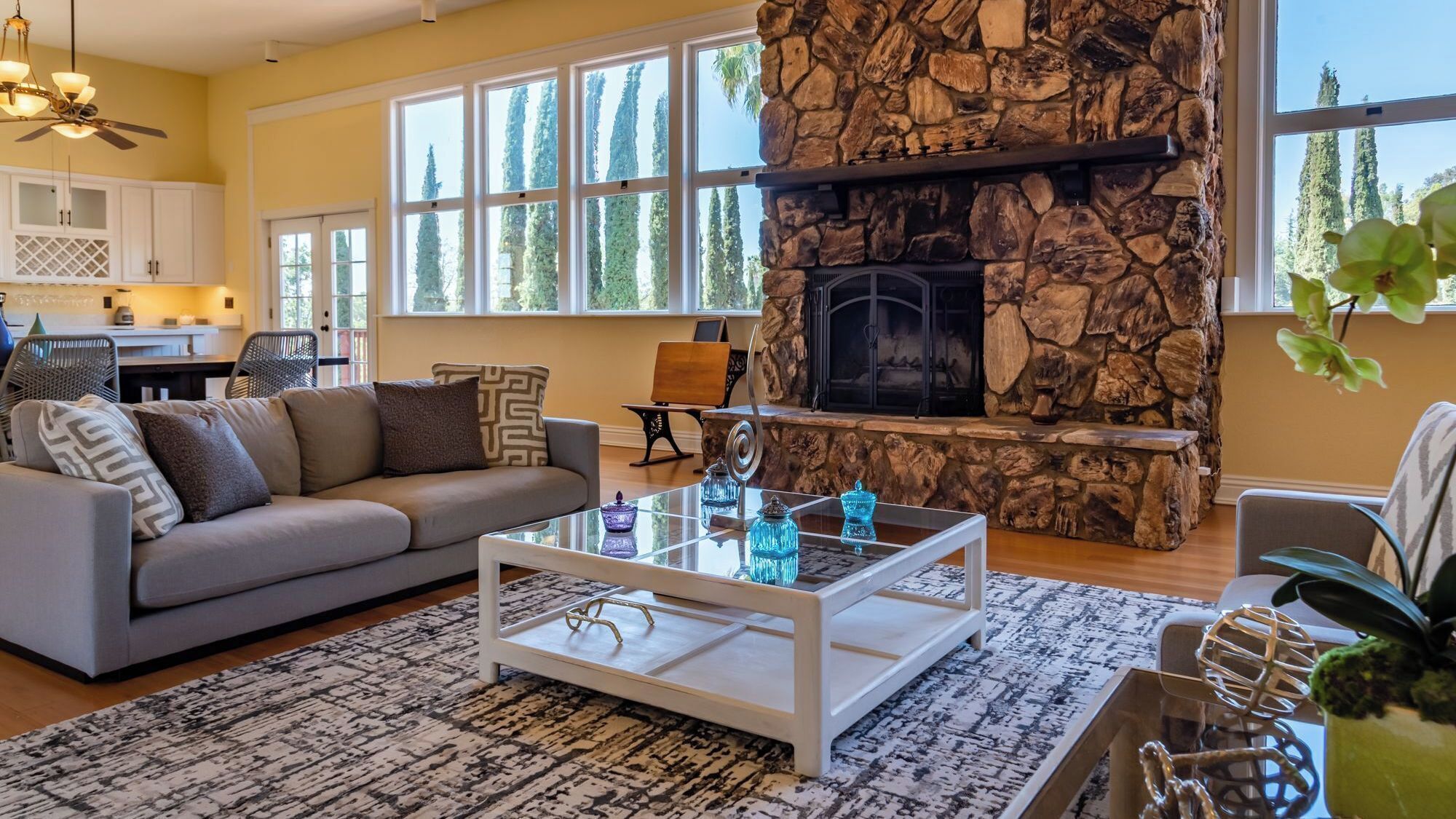 A living room with a stone fireplace, large windows, a sofa, and a coffee table.