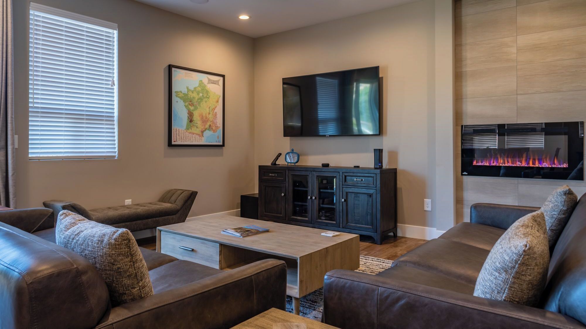 A modern living room with leather sofas, a coffee table, a flat-screen TV, a fireplace, and a map on the wall.
