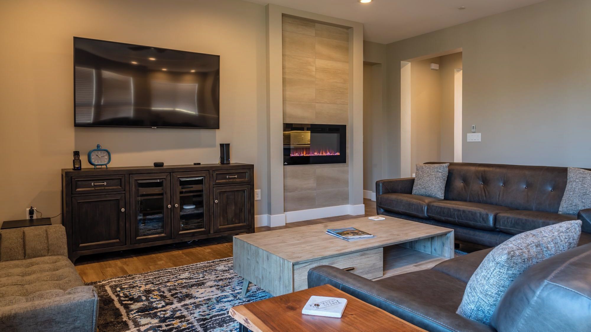 A modern living room with a flat-screen TV, dark wooden cabinet, leather sofa, and a fireplace.