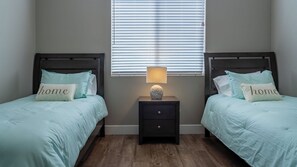 A bedroom with two beds, each with a pillow labeled 'home,' a nightstand with a lamp, and a window with blinds. - Westside Riley House by Avantstay BBQ Deck + Game Lounge Wine Country (Paso Robles)