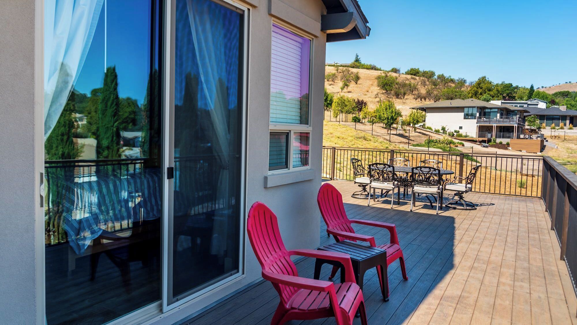 A balcony with red chairs and a table, a sliding glass door, and a view of a hilly landscape.