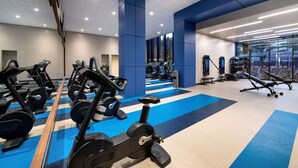 Un gimnasio con diversos equipos de ejercicio, incluyendo cintas de correr y máquinas de pesas, y un suelo con diseño azul y blanco.