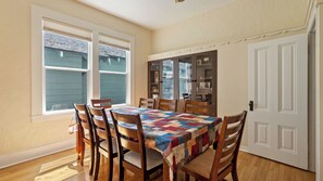 A dining room with a wooden table, chairs, and a colorful quilt. There are two windows and a door. - Vacations on Vine by Avantstay BBQ Yard + Patio Paso Robles Wine Country (Paso Robles)