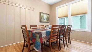 A dining area with a table set for six, wooden chairs, a quilted tablecloth, a framed painting on the wall, and a window with blinds. - Vacations on Vine by Avantstay BBQ Yard + Patio Paso Robles Wine Country (Paso Robles)