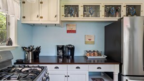 A kitchen with white cabinets, a stainless steel refrigerator, a gas stove, a coffee maker, and a wine glass decoration. - Vacations on Vine by Avantstay BBQ Yard + Patio Paso Robles Wine Country (Paso Robles)