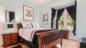 Quarto com uma cama de madeira, uma mesa de cabeceira, um abajur e duas molduras na parede.
