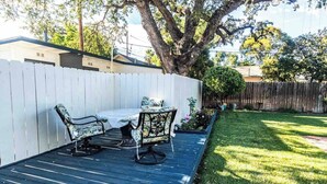An outdoor patio with a table and chairs, surrounded by a white fence, a tree, and a well-maintained lawn. - Vacations on Vine by Avantstay BBQ Yard + Patio Paso Robles Wine Country (Paso Robles)