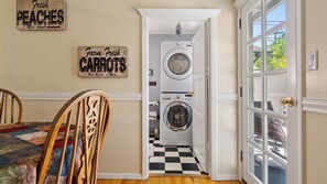 A laundry room with two washing machines, a checkered floor, and a door leading to a dining area with a table and chairs. - Vacations on Vine by Avantstay BBQ Yard + Patio Paso Robles Wine Country (Paso Robles)