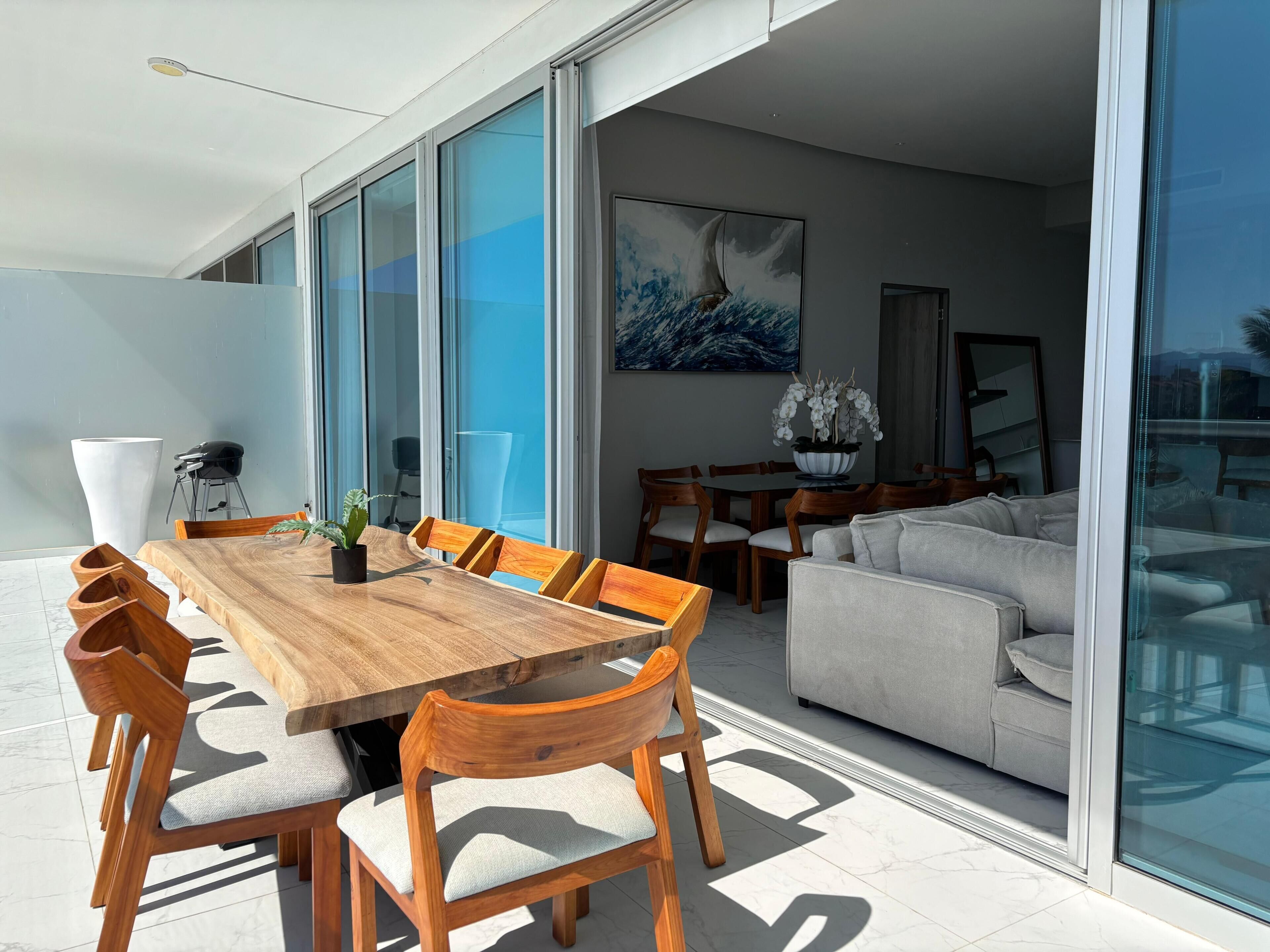 Un espace repas moderne avec une table et des chaises en bois, un canapé et une grande fenêtre.