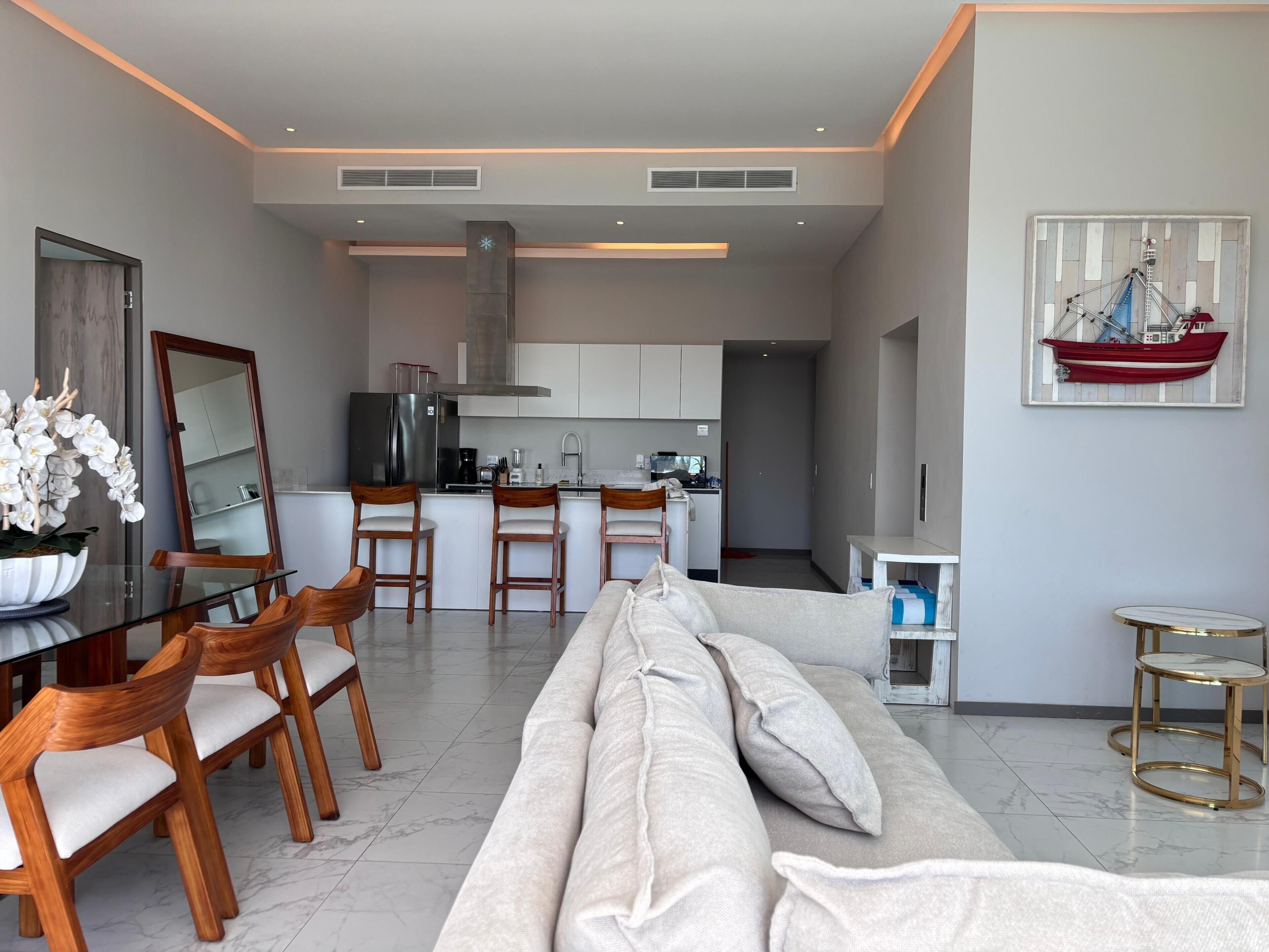 Un salon moderne avec un canapé, une table à manger, des chaises et une cuisine en arrière-plan.