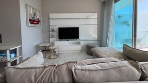 A modern living room with a flat-screen TV, a sofa, a coffee table, and a large window. - Apartment in New Vallarta (Nayarit)