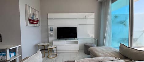 Una sala de estar moderna con un televisor de pantalla plana, un sofá, una mesa de centro y un ventanal grande.