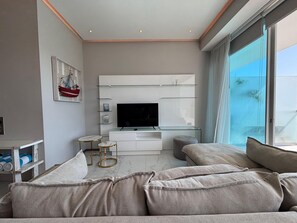 A modern living room with a flat-screen TV, a sofa, a coffee table, and a large window. - Apartment in New Vallarta (Nayarit)