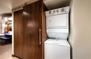 A hotel room with a wooden wardrobe, a white washing machine, and a bed with a blue headboard.