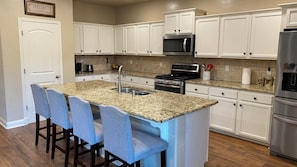 A kitchen with white cabinets, a granite countertop, a stainless steel refrigerator, and a built-in microwave. - Sequoia comfort (Visalia)