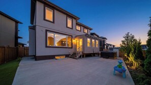 A modern two-story house with a covered patio, a staircase leading to the upper floor, and a well-maintained lawn. - The Solstice Estate: Hot Tub, Bar & 2 King Suites (Edmonton)