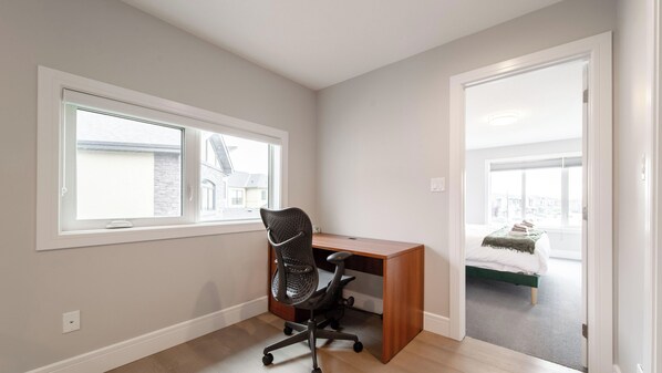 A room with a wooden desk, a black office chair, a window, and a door leading to another room. - The Solstice Estate: Hot Tub, Bar & 2 King Suites (Edmonton)