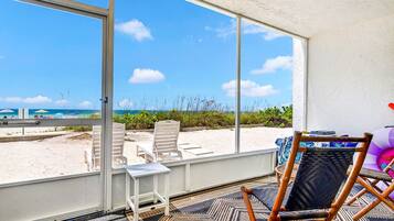 A room with a large window overlooking a beach, a small table, and a wicker chair.