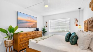 A bedroom with a bed, wooden dresser, and a large window with blinds.