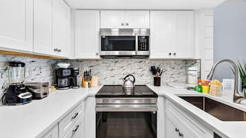 A modern kitchen with white cabinetry, a stainless steel microwave, a kettle, and various appliances.